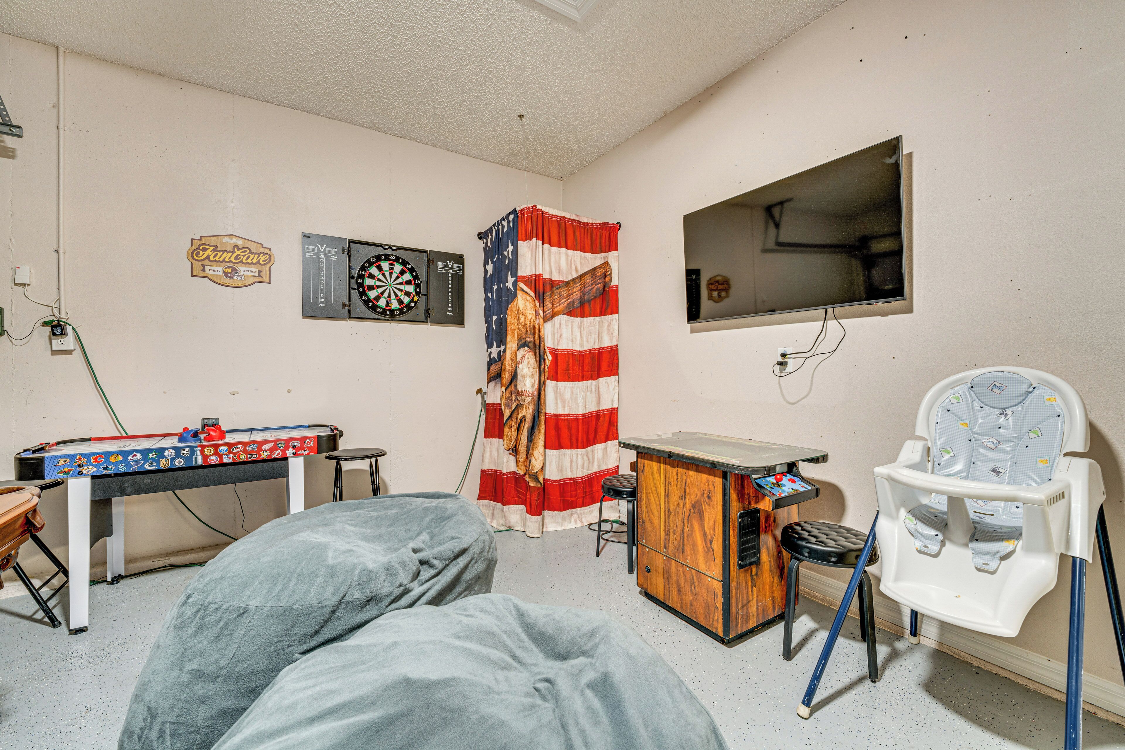 Ein Zimmer mit Dartscheibe, Kicker, Babybett und Fernseher.