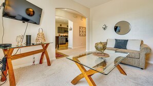 A living room with a TV, glass coffee table, sofa, and a kitchen in the background. - 11 Mi to Disney: Home w/ Pool in Davenport! (Davenport)