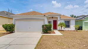 A single-story house with a white garage door, a red front door, and a small front yard with a palm tree and shrubs. - 11 Mi to Disney: Home w/ Pool in Davenport! (Davenport)
