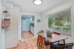 A kitchen with white cabinets, a dining table with chairs, a window with blinds, and a tiled floor.