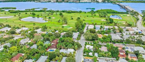 An aerial view of a coastal residential area with houses, a golf course, and a marina.