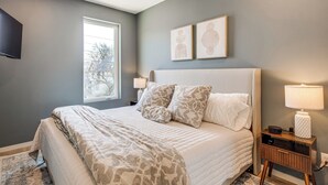 Une chambre à coucher avec un lit, une table de chevet, une lampe et deux tableaux encadrés accrochés au mur.