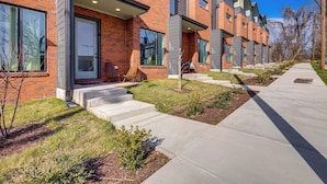 Une rangée de maisons de ville modernes en briques, dotées de grandes fenêtres, d’un chemin en béton et d’un petit espace jardin.