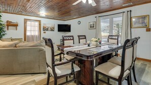 A dining area with a wooden ceiling, a television mounted on the wall, and a dining table set with chairs.