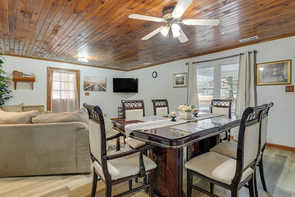 A dining area with a wooden ceiling, a television mounted on the wall, and a dining table set with chairs.