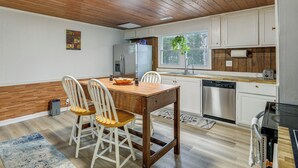 A kitchen with wooden ceiling, white cabinets, a wooden dining table with chairs, a refrigerator, and a dishwasher.