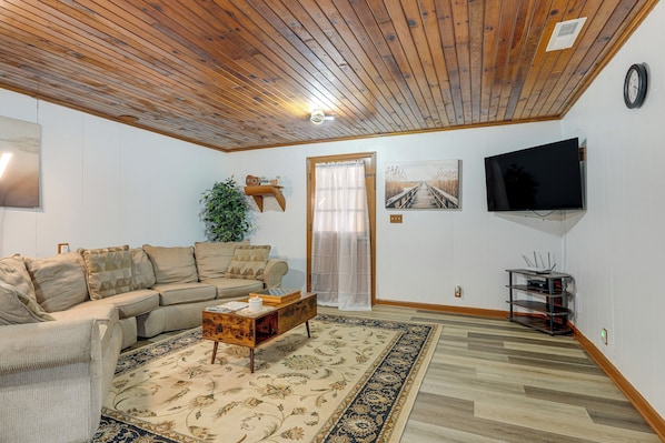 Una sala de estar con techo de madera, un sofá, una mesa de centro, un televisor y una planta.