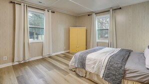 A bedroom with a bed, wooden flooring, a yellow wardrobe, and large windows.