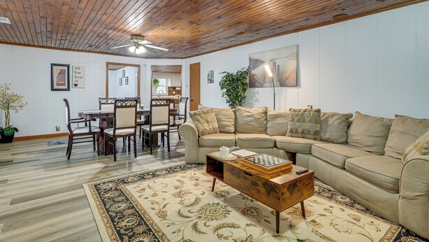 A living room with a wooden ceiling, a beige sofa, a coffee table, and a dining area with chairs and a table.