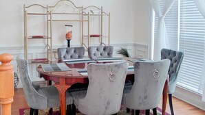 Un coin repas comprenant une table ronde, six chaises grises à revêtement rembourré, un présentoir en métal doré avec des étagères et un tapis à motifs.