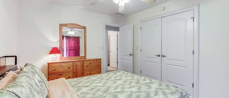A bedroom with a bed, a dresser, a mirror, a ceiling fan, and white doors.