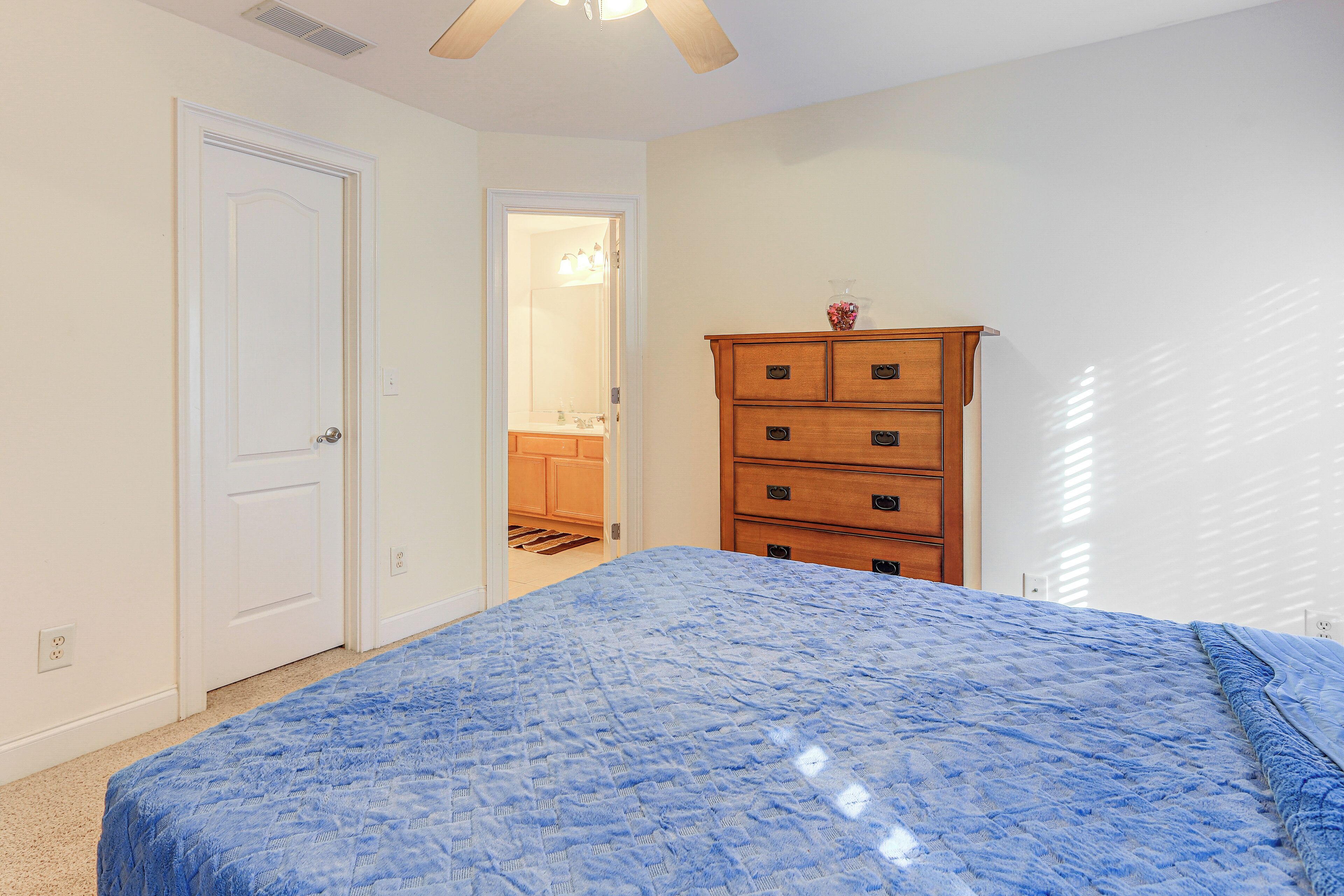 A bedroom with a bed, a wooden dresser, and a door leading to a bathroom.