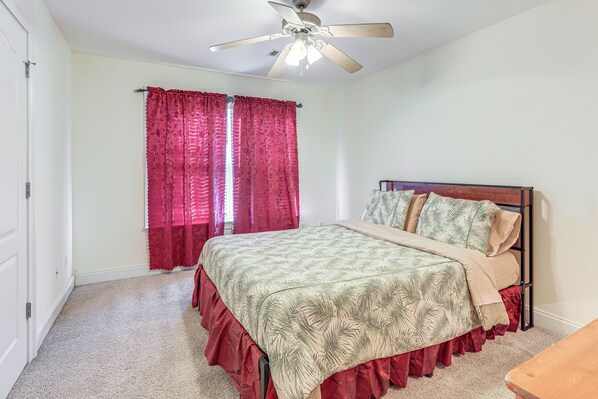 A bedroom with a bed, a ceiling fan, and a window with red curtains.
