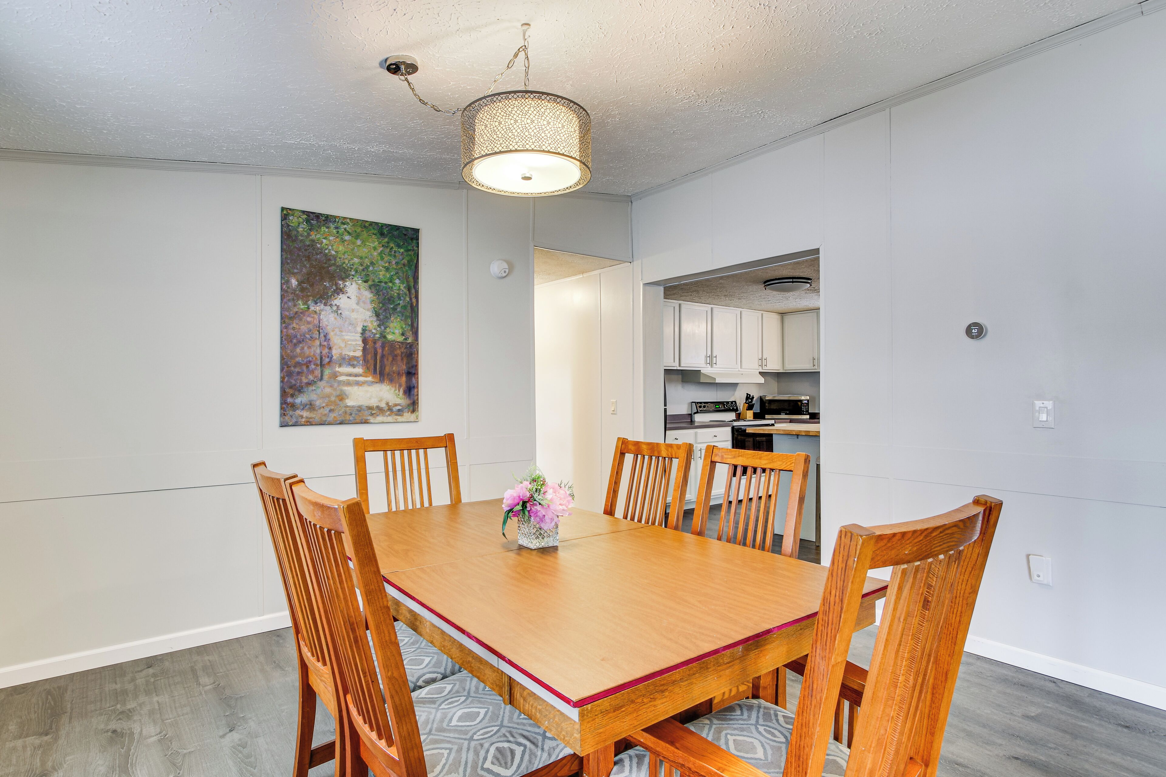 A dining area with a wooden table and chairs, a vase with flowers, and a painting on the wall.
