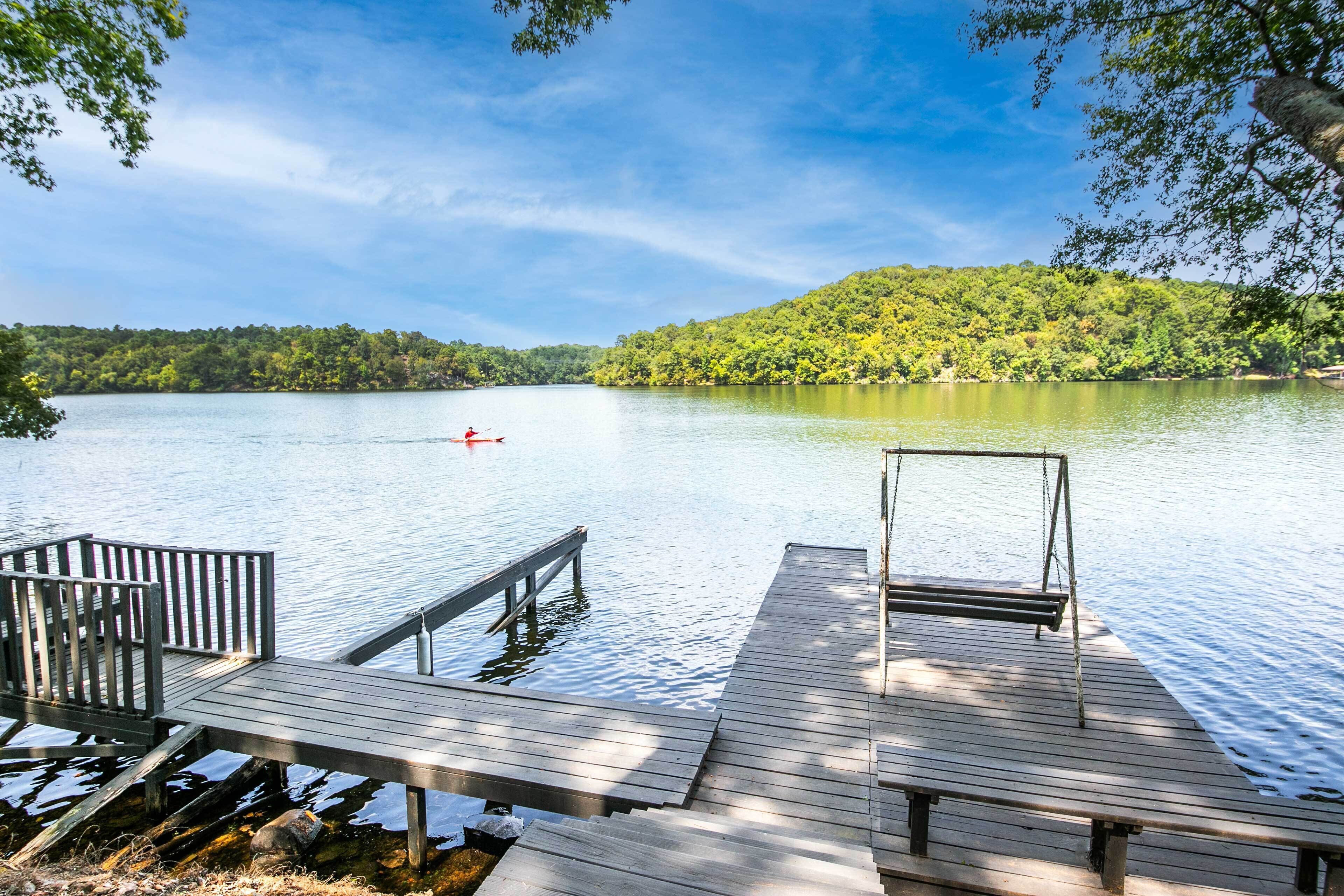 A wooden dock extending into a calm lake with a forested hill in the background.