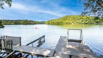 A wooden dock extending into a calm lake with a forested hill in the background.