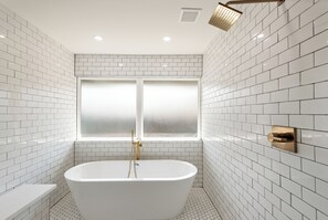 Un baño moderno con azulejos blancos tipo metro, una bañera independiente y un ventanal con vidrio esmerilado.