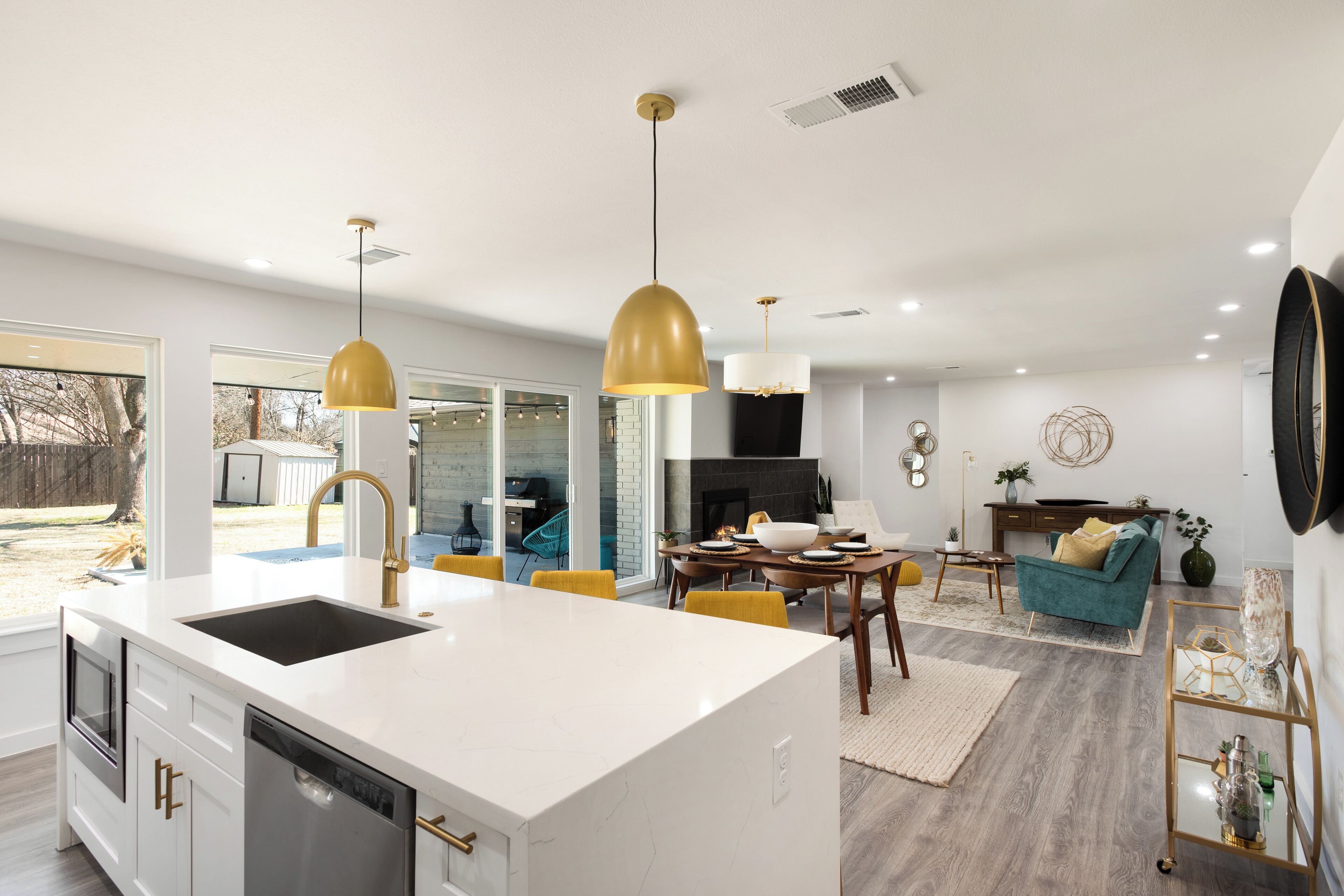 A modern kitchen with a central island, a dining area with a wooden table, and a living room with a sofa and decorative items.