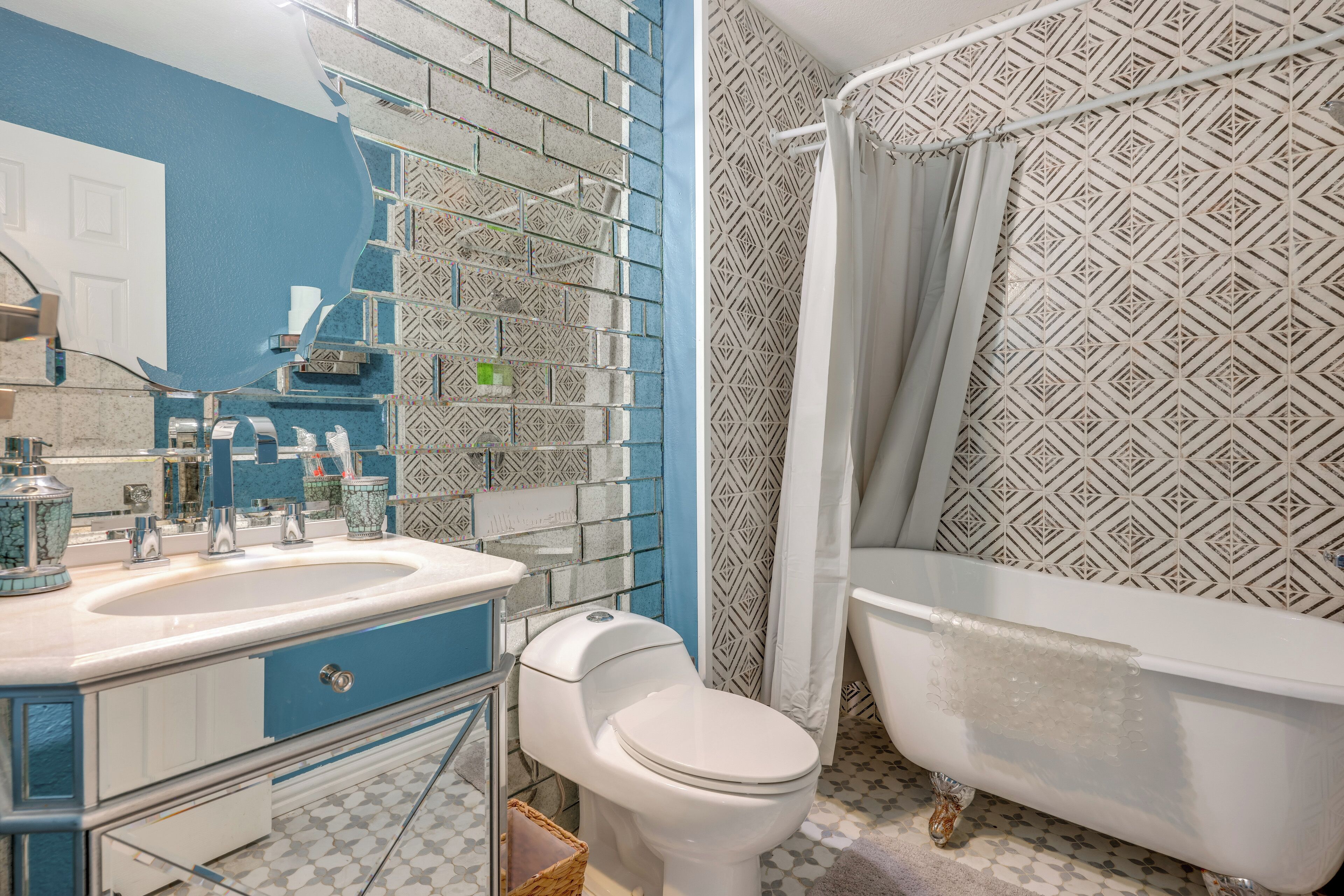 Une salle de bain avec des toilettes blanches, un lavabo avec un meuble bleu et une baignoire agrémentée d’un rideau de douche à motifs.