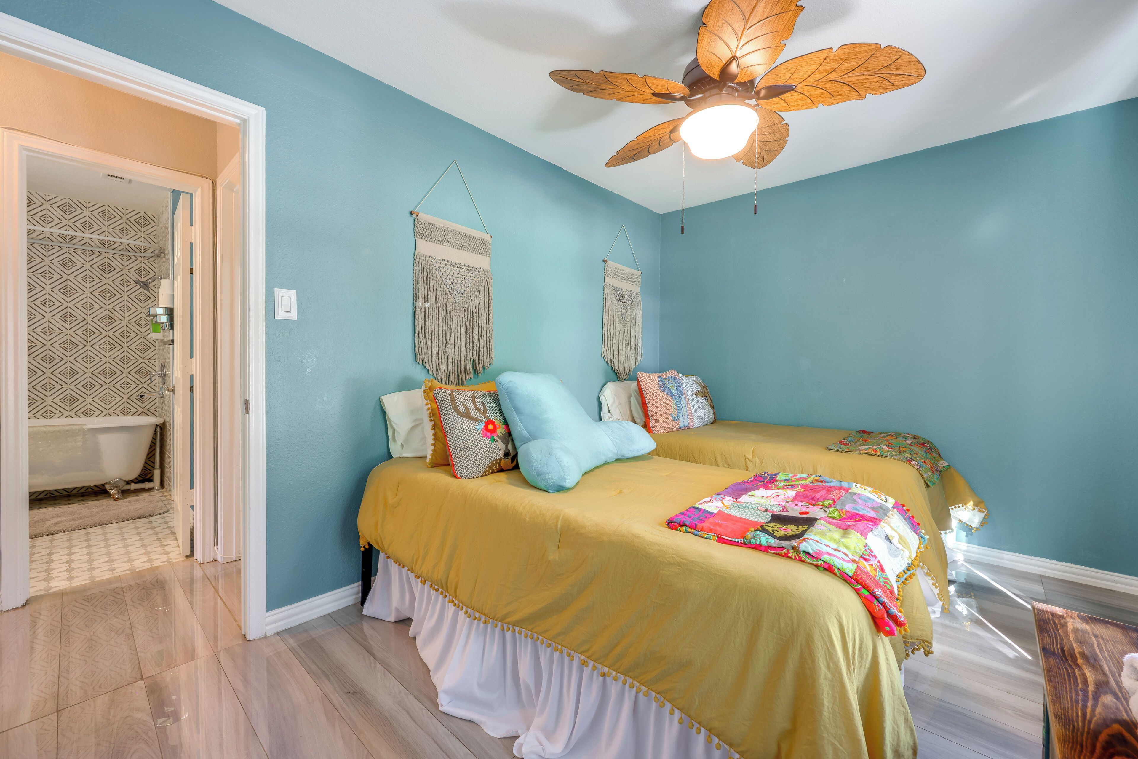 A bedroom with two beds, a ceiling fan, and a bathroom with patterned tiles.