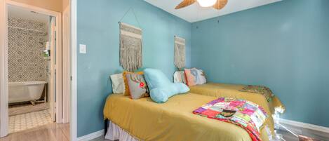 A bedroom with two beds, a ceiling fan, and a bathroom with patterned tiles.