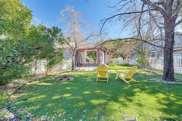 Ein Garten mit Glasveranda, zwei gelbe Adirondack-Stühle und ein Baum.