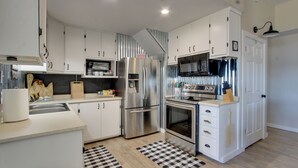 Een moderne keuken met witte kasten, roestvrijstalen apparatuur en geruite vloerkleden.