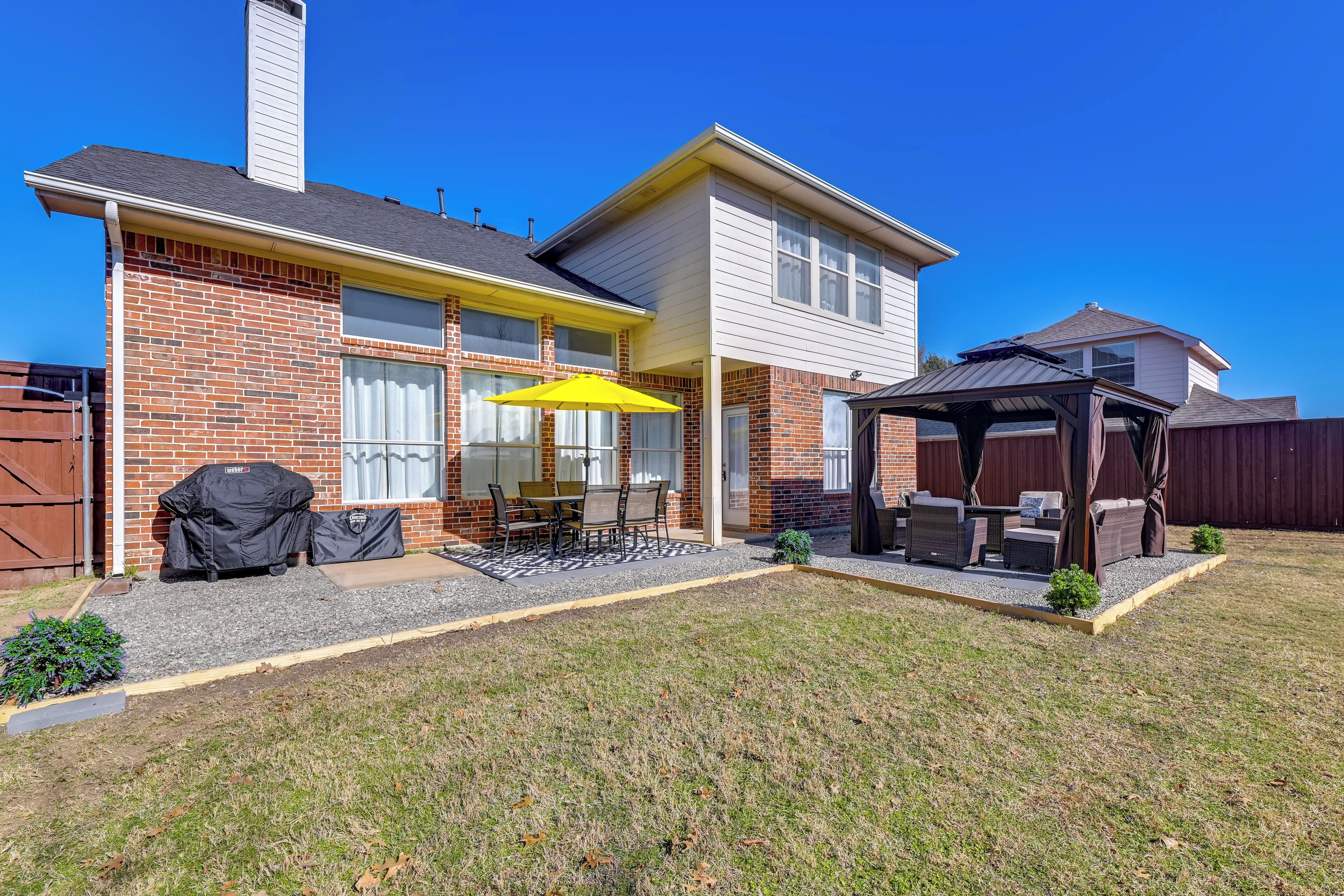 A two-story house with a patio area featuring outdoor furniture and a yellow umbrella.