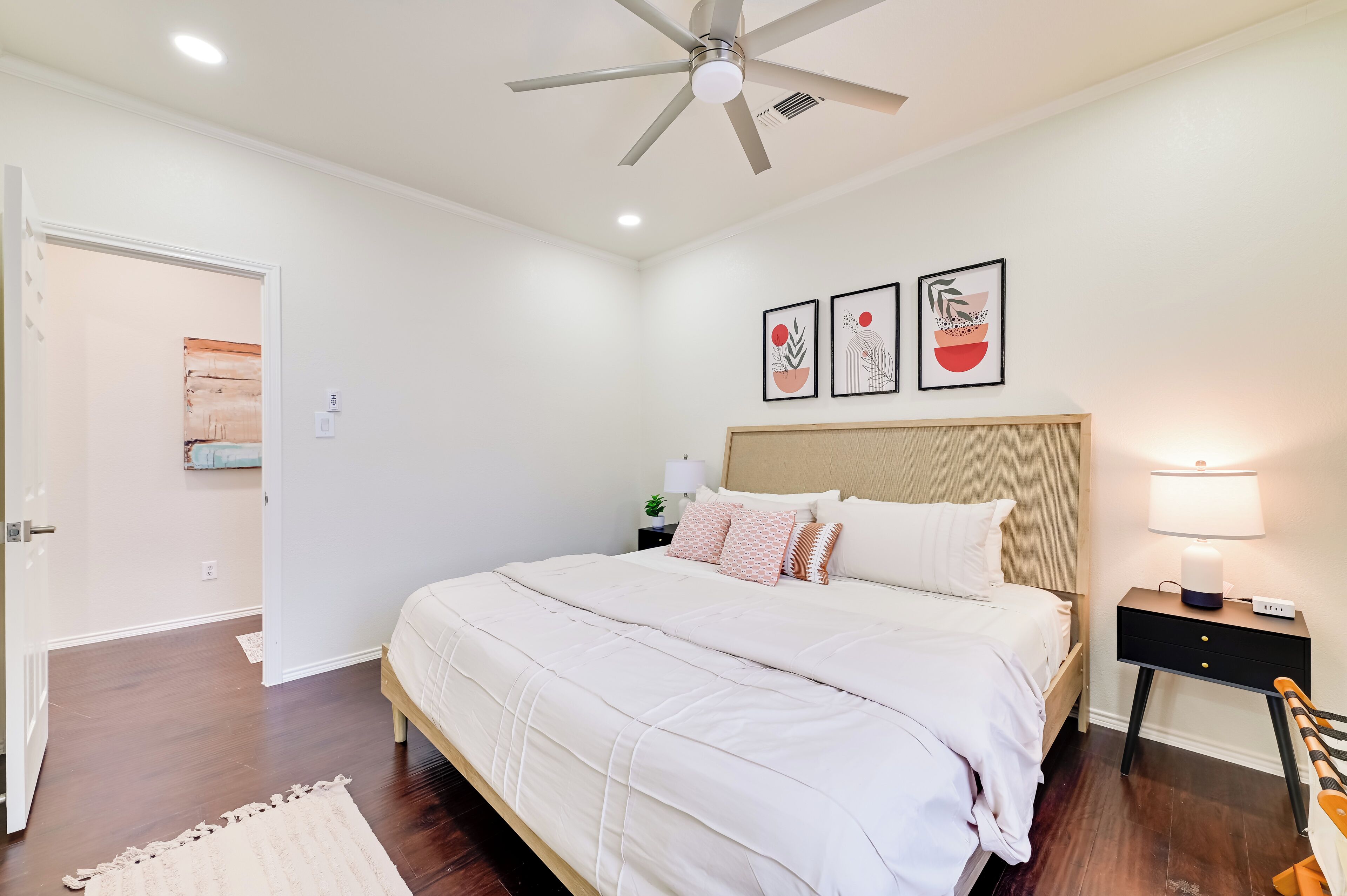 A bedroom with a bed, a nightstand, a ceiling fan, and wall art.