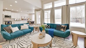 A modern living room with teal sofas, a round coffee table, and a kitchen in the background. - 4 Mi to Dtwn: Family Home w/ Games in Frisco (Frisco)