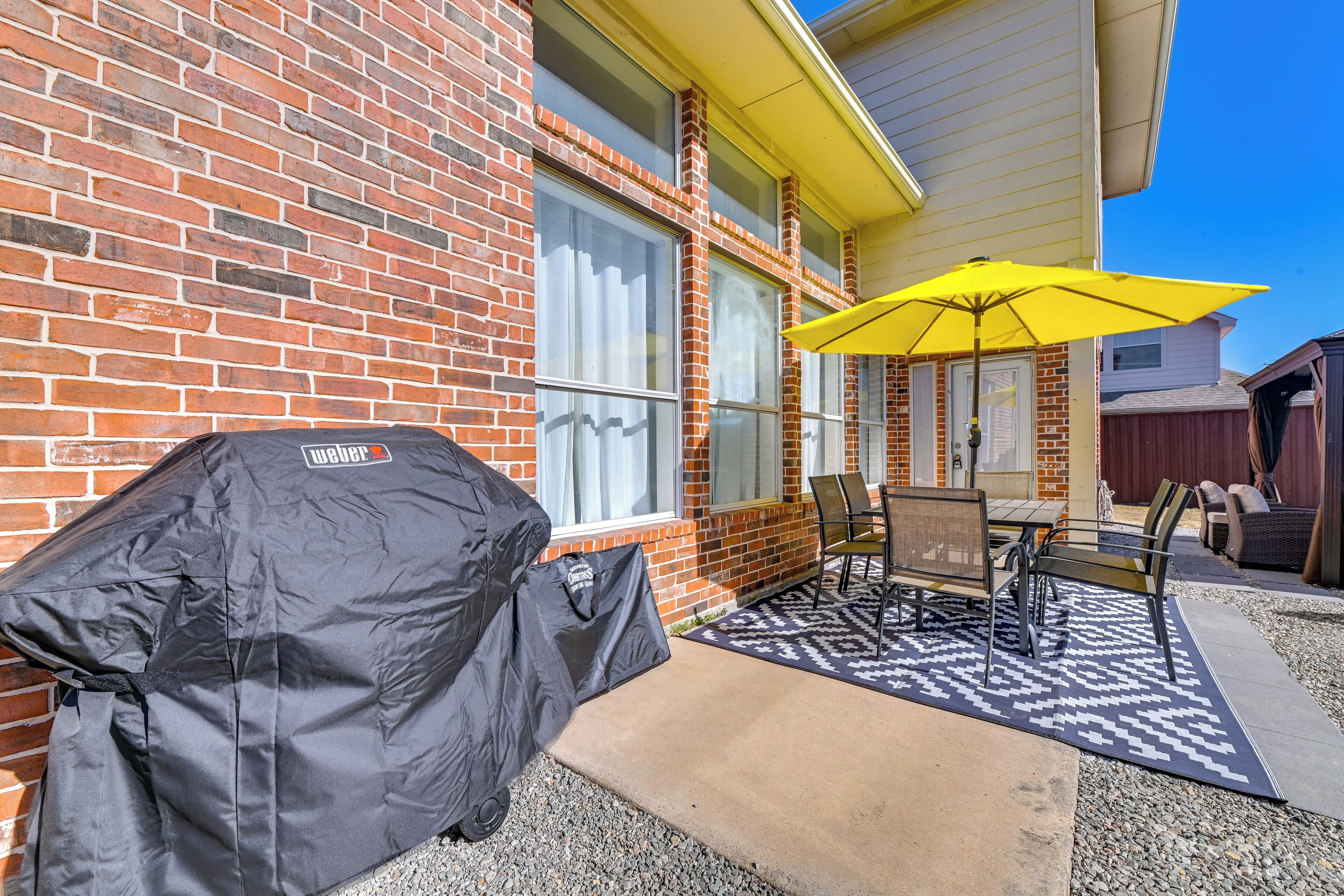 A patio with a grill, outdoor furniture, and a yellow umbrella.