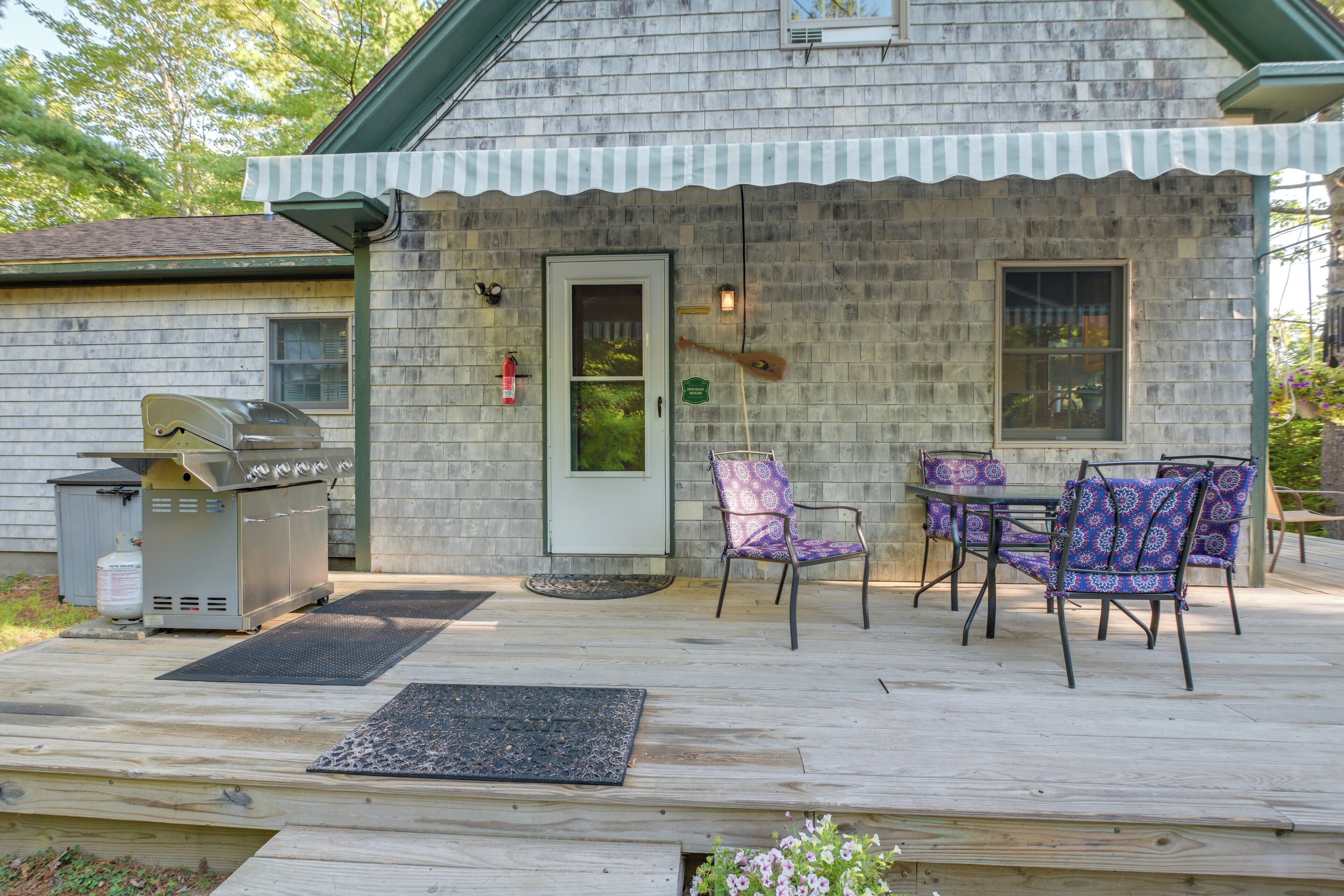 Une terrasse en bois avec des meubles d’extérieur, un barbecue et une porte donnant sur un petit espace de véranda.