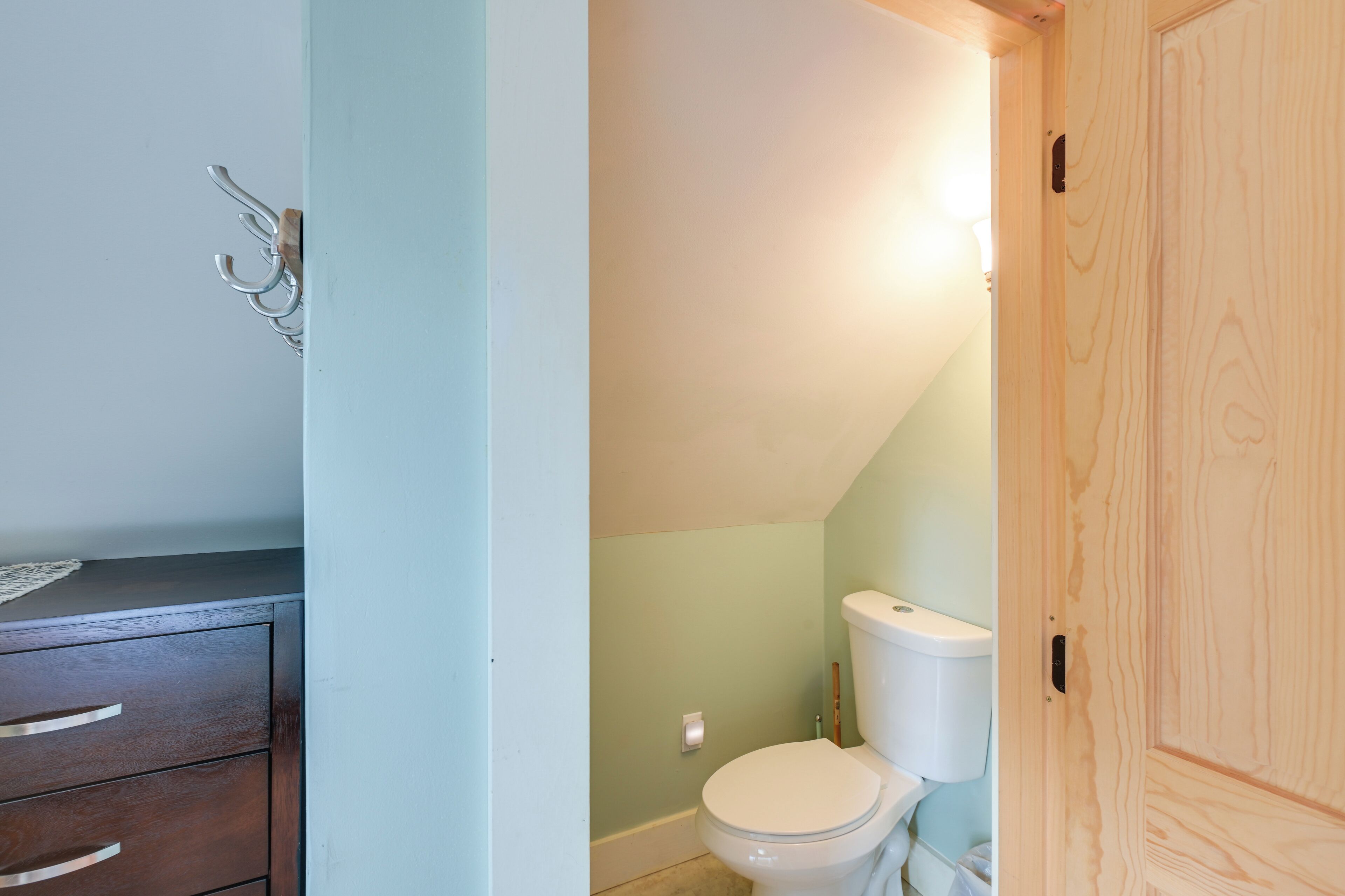 Un baño con puerta de madera, inodoro blanco y mueble de madera con cajones.