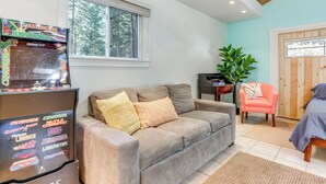 A living room with a beige sofa, a retro arcade machine, a potted plant, and a wooden door. - Drive to Major Parks: Nature Getaway in West Point (West Point)