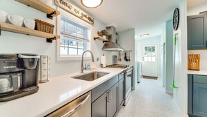 A modern kitchen with a built-in dishwasher, a coffee maker, and a sink. There are wooden shelves above the counter and a window with blinds. - Walk to Lakemont Park: Family-friendly Home! (Altoona)