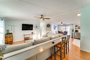 Un salon moderne avec un long canapé gris, une table basse en bois et un ventilateur de plafond.