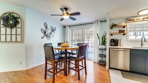 A dining area with a round table and chairs, a ceiling fan, a kitchen with a dishwasher, and a window with curtains. - Walk to Lakemont Park: Family-friendly Home! (Altoona)