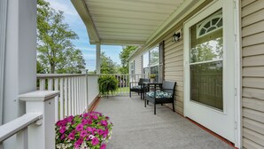 A covered porch with a white railing, a seating area with chairs, and a potted plant with flowers. - Walk to Lakemont Park: Family-friendly Home! (Altoona)