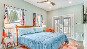 A bedroom with a bed, two bedside tables, a window with curtains, a ceiling fan, and a door.