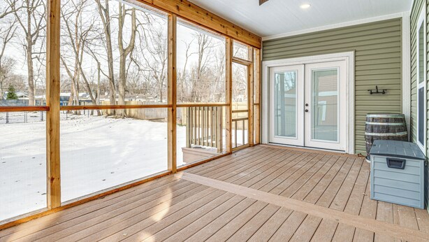 A covered porch with large windows, a ceiling fan, and a view of a snowy yard.