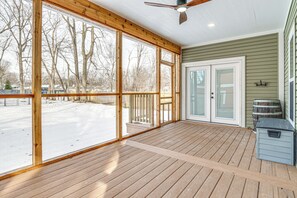 Ein überdachter Balkon mit großen Fenstern, einem Deckenventilator und Blick auf einen verschneiten Garten.