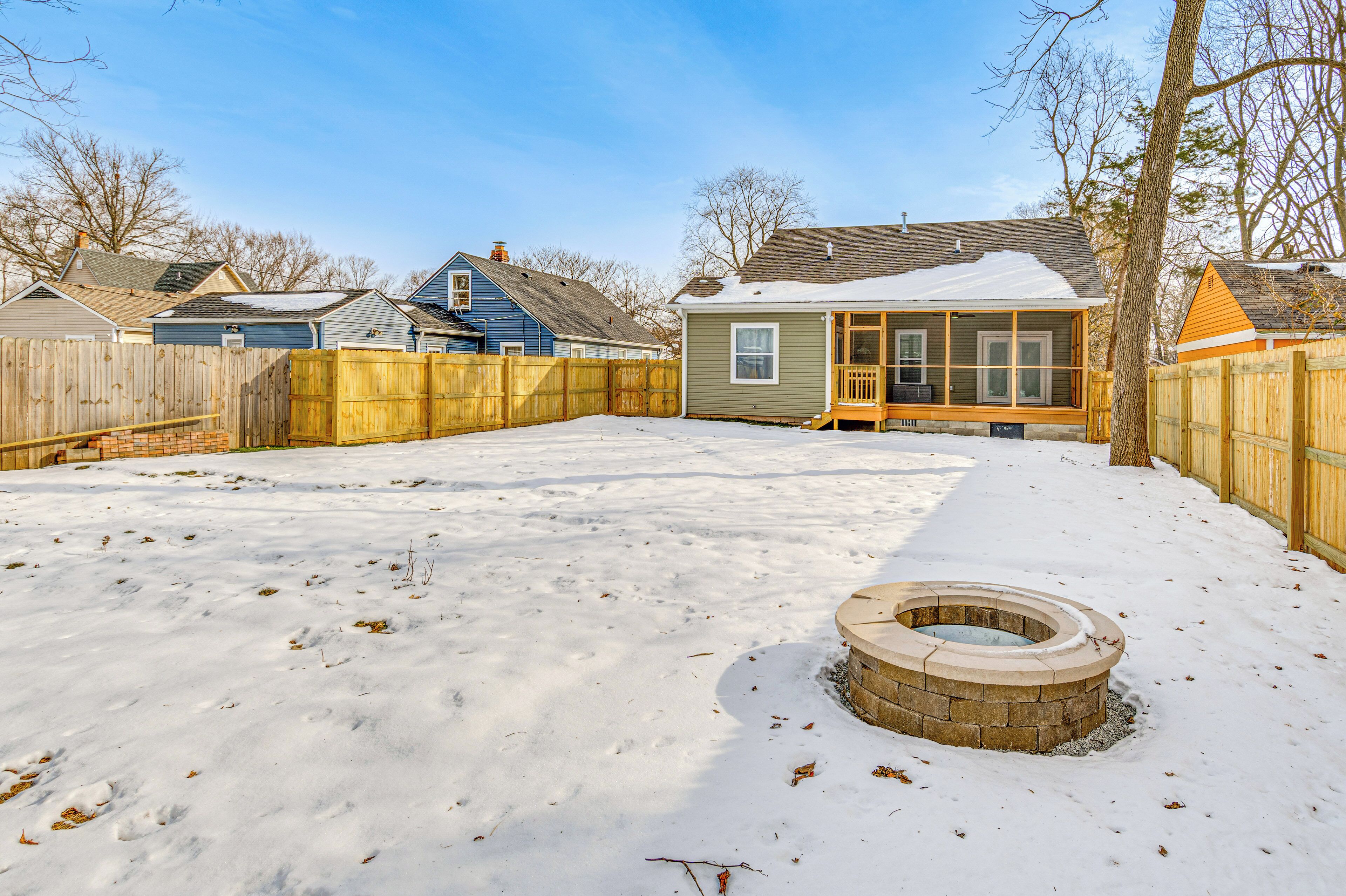 A backyard with a wooden deck, a fire pit, and a house with a porch.