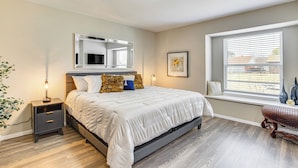 A bedroom with a bed, bedside tables, a nightstand, a window with blinds, and a wall-mounted mirror. - 5 Mi to Fort Worth Stockyards: Home w/ Yard! (Haltom City)