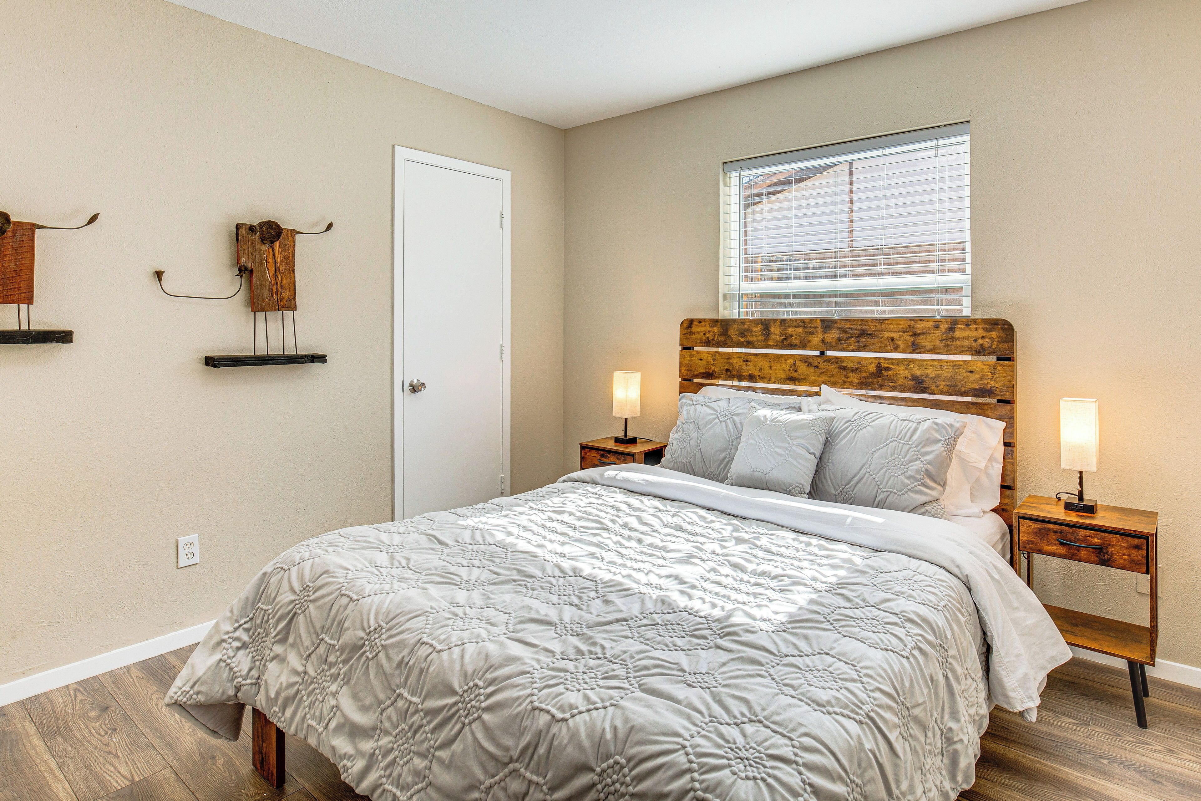 A bedroom with a large bed, wooden headboard, bedside lamps, and a window with blinds.