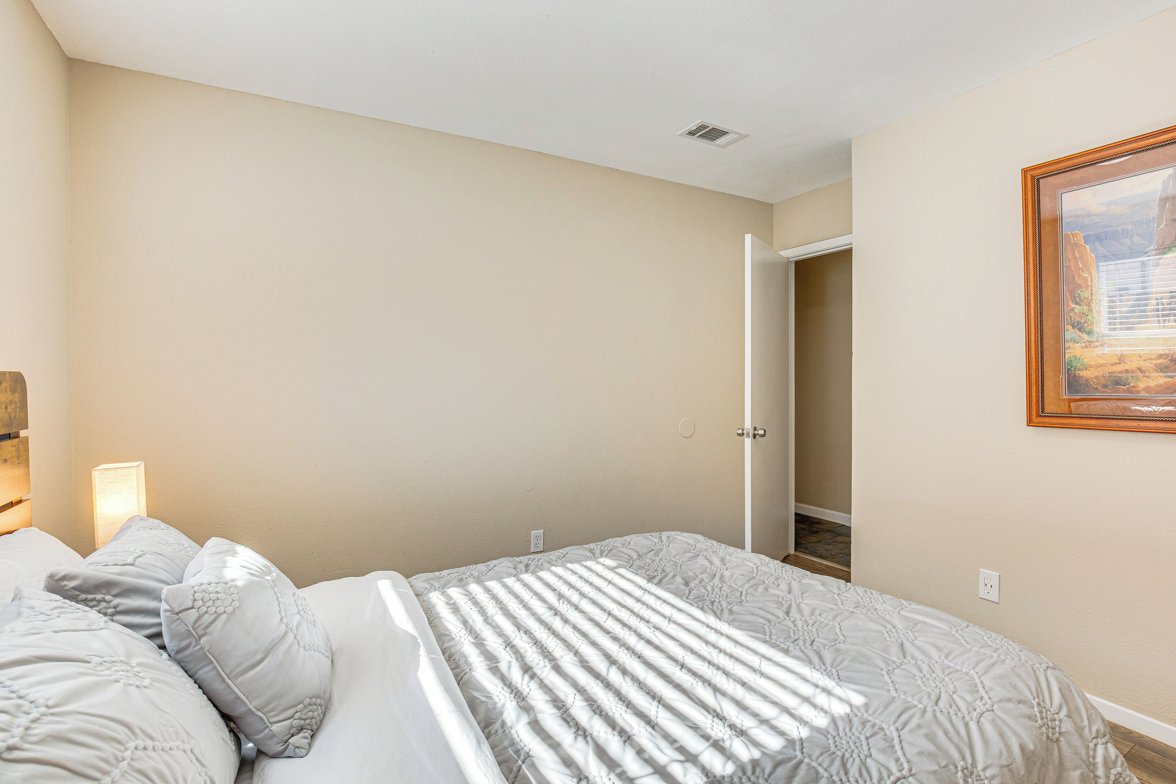 A bedroom with a bed, a nightstand, a lamp, and a painting on the wall.