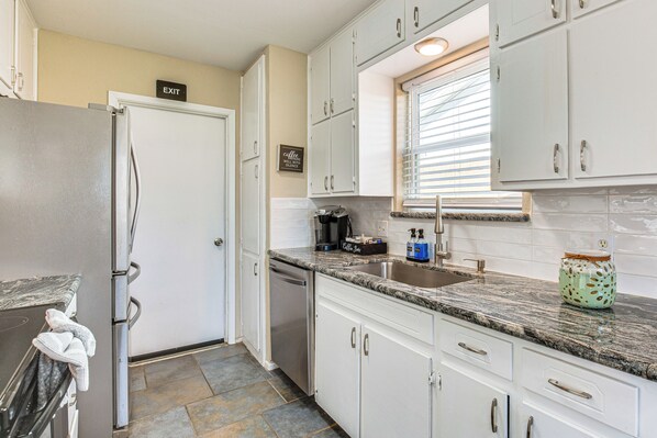 A kitchen with white cabinets, a granite countertop, a coffee maker, and a window with blinds. - 5 Mi to Fort Worth Stockyards: Home w/ Yard! (Haltom City)
