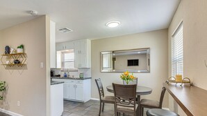 A compact kitchen with white cabinets, a dining area with a round table and chairs, and a large mirror above the counter. - 5 Mi to Fort Worth Stockyards: Home w/ Yard! (Haltom City)