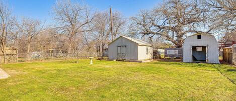 A rural property with a large open grassy area, a small white shed, and a larger barn-like structure.