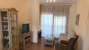 A living room with a television, a cabinet with glass doors, a fireplace, and a wicker chair. - Ideal for family trips, close to Rocio and Portugal, pets welcome. (Islantilla)