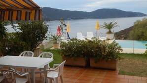 Un patio con mesa y sillas, con vista a un cuerpo de agua y colinas.